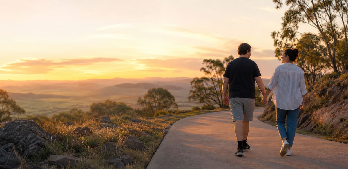 A support worker and participant walking hand in hand along a winding path at sunset in the Queensland hills